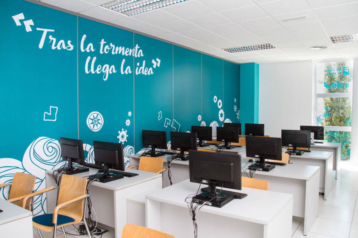 Computer room of the IMFE project with spatial branding on turquoise walls, inspirational phrase in large format and computer stations distributed in rows.